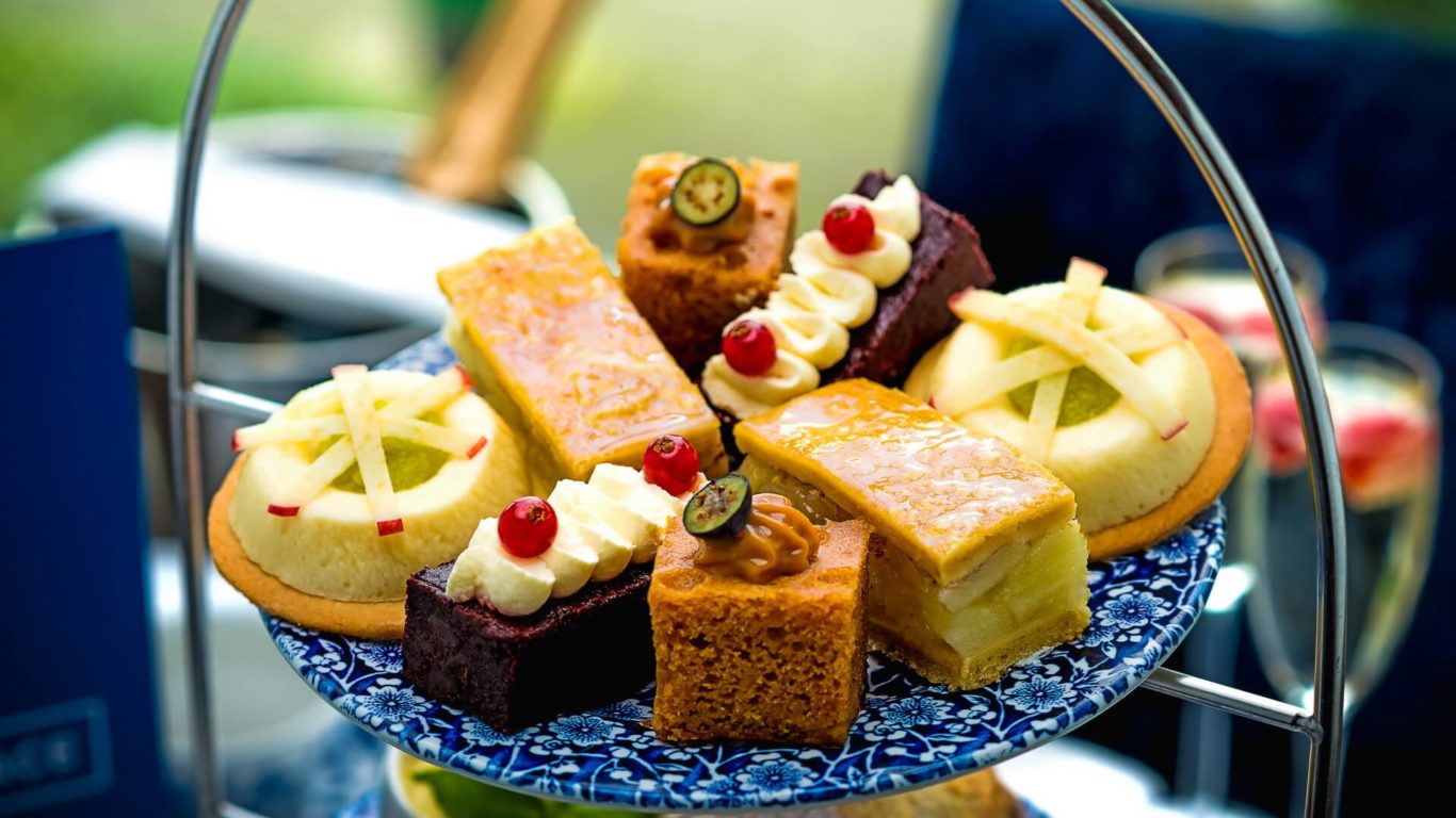 An assortment of colorful pastries, cakes, and tarts with fruit and cream toppings arranged on a blue-patterned tiered tray.