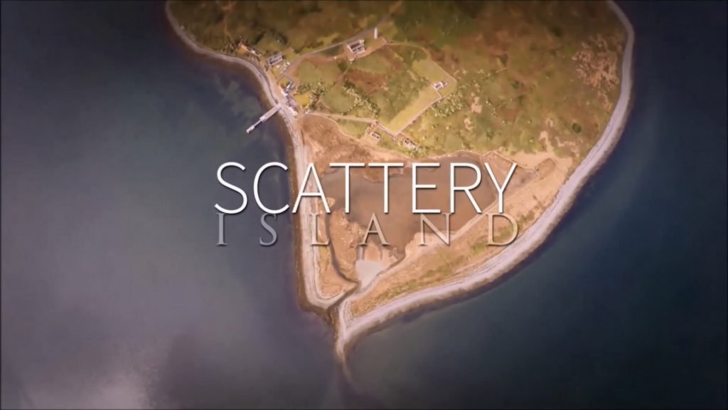 Aerial view of Scatterly Island coastline with scattered buildings, grass, and roads; text overlay reads 