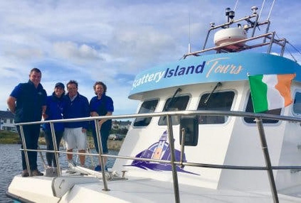 Four people stand on the deck of a boat labeled 