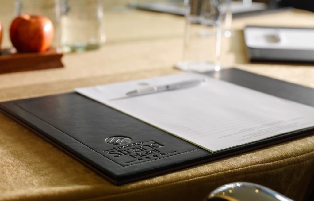 A notepad and pen on a black leather folder embossed with 