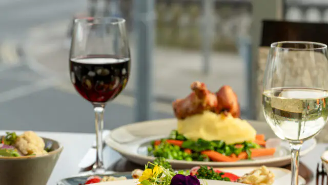 A table set with plates of gourmet food, a glass of red wine, a glass of white wine, and a city street visible through the window in the background.