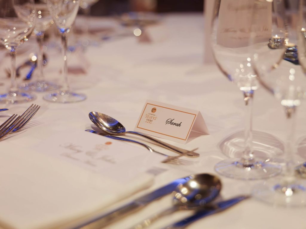 A formal dining table set with glassware, cutlery, and place cards, including one with the name 