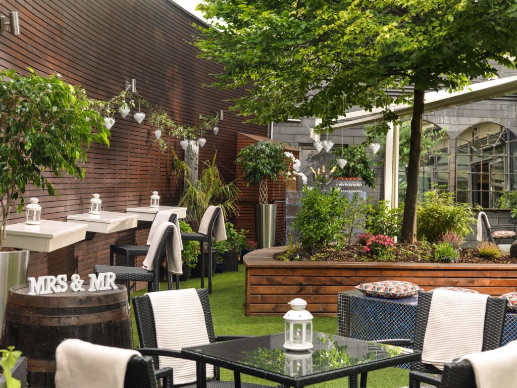 Outdoor seating area with glass tables, chairs, potted plants, and a 
