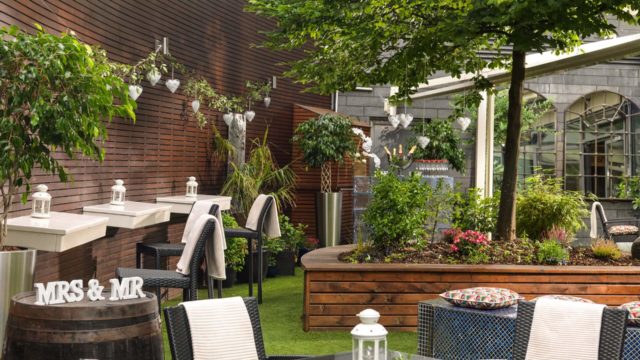 Outdoor seating area with glass tables, chairs, potted plants, and a