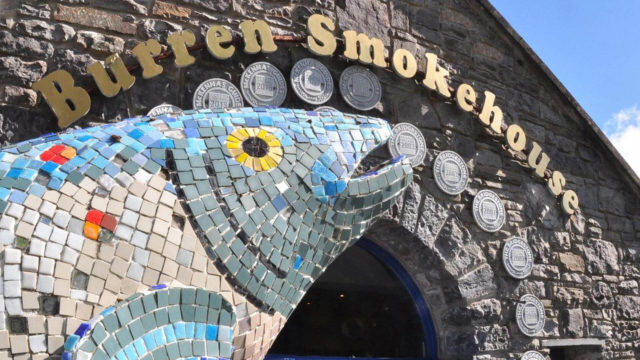 Mosaic fish sculpture in front of the Burren Smokehouse entrance with award plaques displayed on the stone wall.