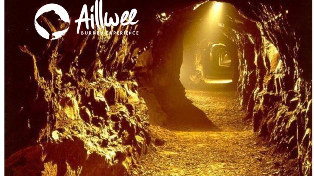 A rocky tunnel inside a cave is illuminated by artificial yellow lighting, with the 