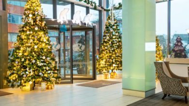 Lobby decorated for Christmas with lit Christmas trees, wrapped presents, and polar bear figures above a glass revolving door.