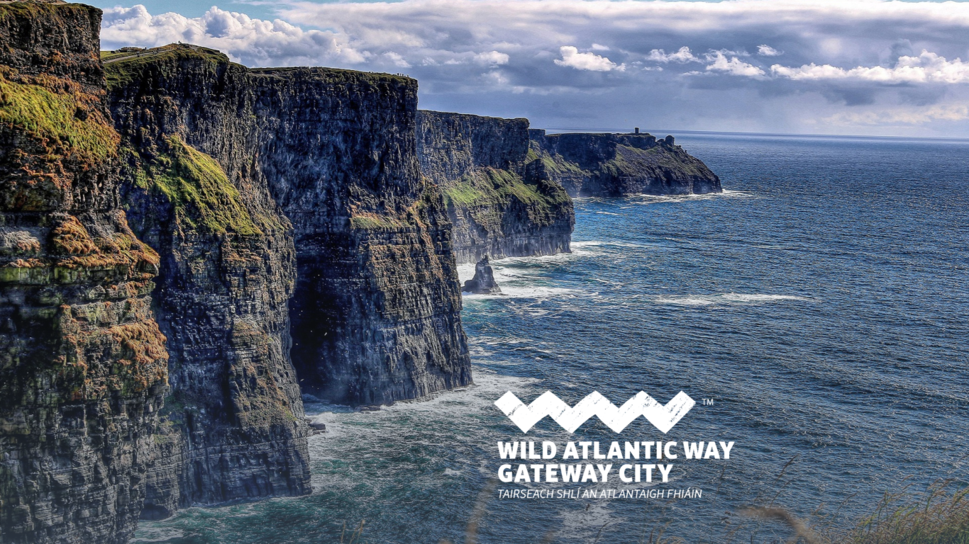 Cliffs rise sharply above the Atlantic Ocean under a partly cloudy sky, with the 