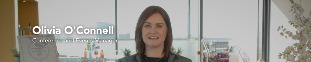 A woman stands indoors in front of large windows, with the text 