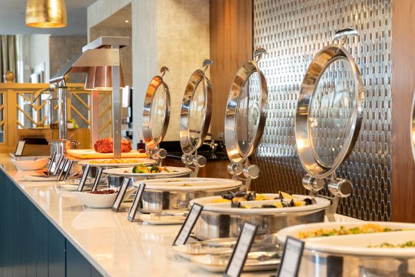A buffet station with several chafing dishes containing various hot foods, each with a label, set on a white countertop.