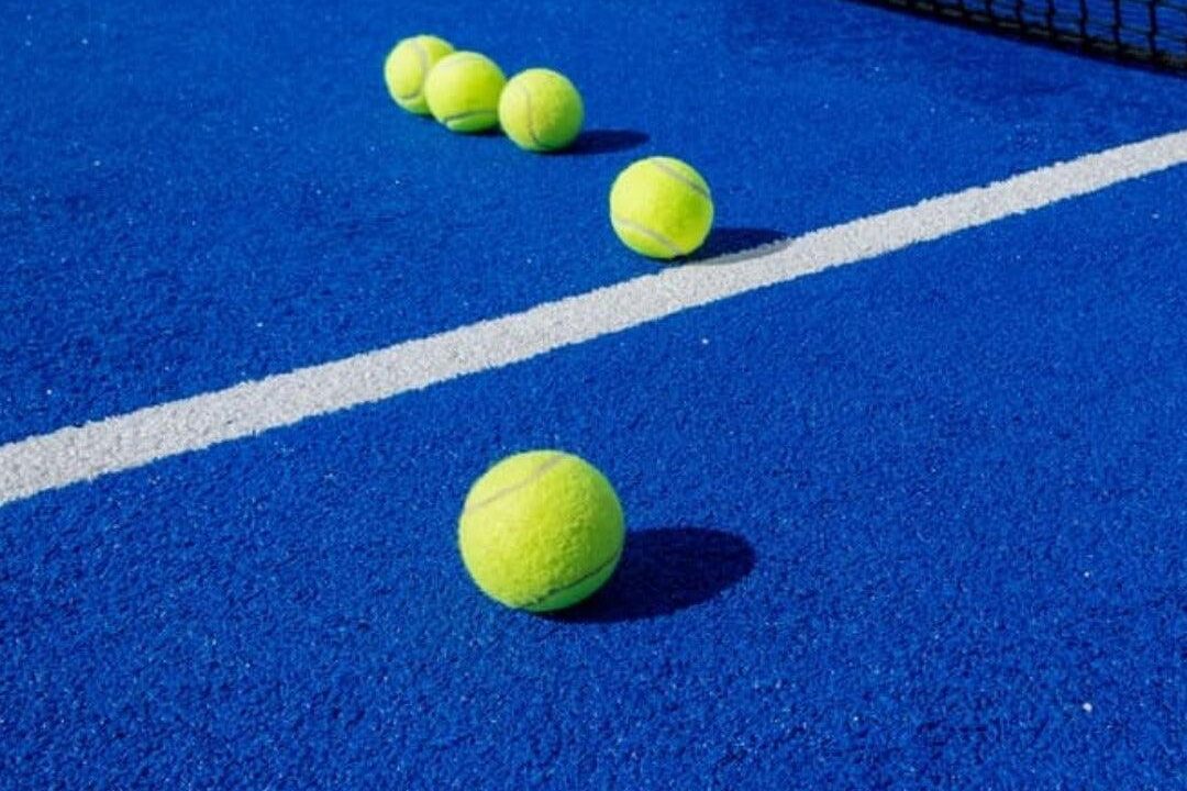 Several tennis balls are scattered on a bright blue tennis court near the net, with a white line visible on the surface.