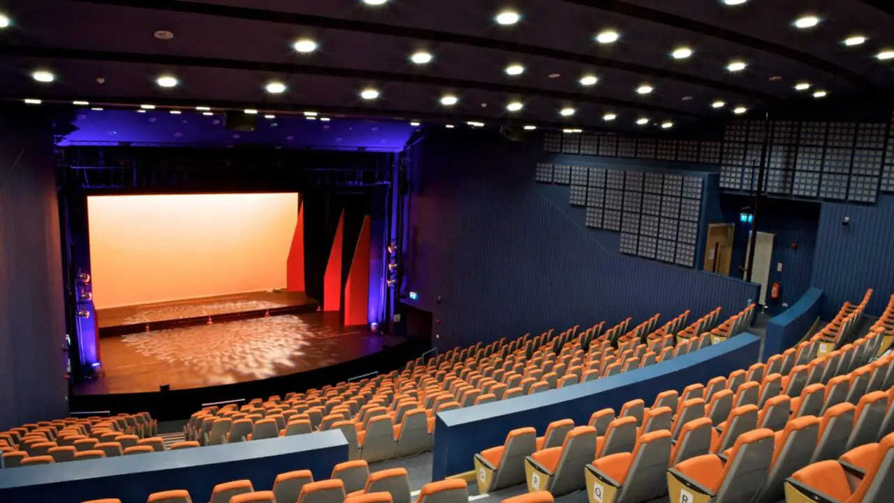 interior view of the Lime Tree Theatre in Limerick, featuring tiered orange seating and a professionally lit stage with orange and blue spotlights.