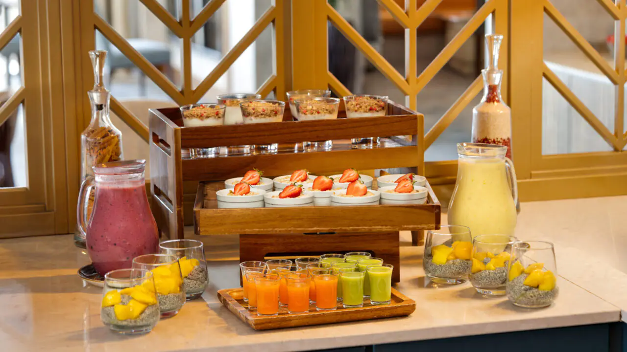 A buffet table with chia pudding, fruit smoothies, layered desserts, and parfaits, all arranged in glass cups and wooden trays on a marble countertop.