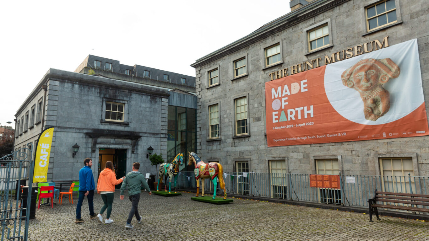 Four people walk toward the entrance of The Hunt Museum, which displays a large banner for the 
