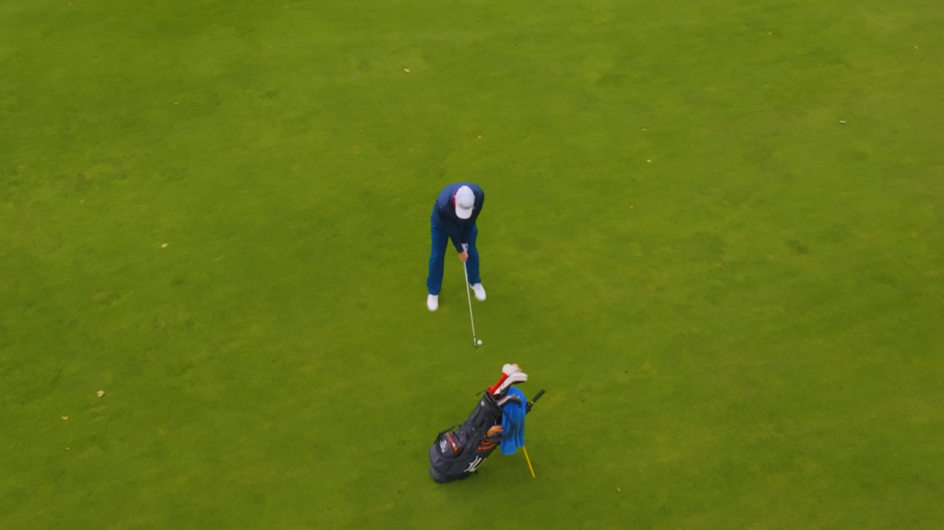 A person in blue sportswear prepares to hit a golf ball on a green field, with a golf bag nearby.
