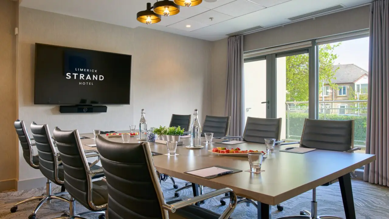 Modern conference room with a long table, leather chairs, wall-mounted screen displaying 