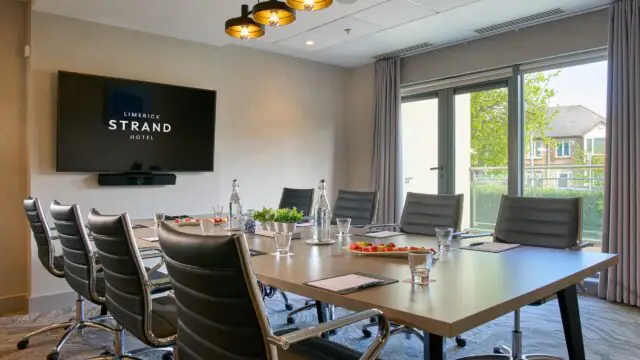 Modern conference room with a long table, leather chairs, wall-mounted screen displaying